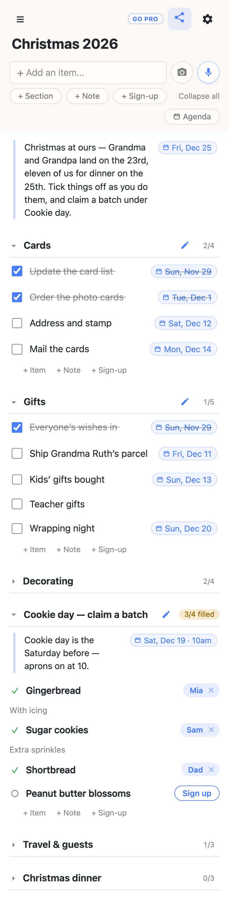 A phone showing a list titled “Christmas 2026”. A note at the top, with a date chip reading Fri, Dec 25, says: Christmas at ours — Grandma and Grandpa land on the 23rd, eleven of us for dinner on the 25th. Tick things off as you do them, and claim a batch under Cookie day. The Cards section reads 2/4: Update the card list (Sun, Nov 29) and Order the photo cards (Tue, Dec 1) are ticked and struck through; Address and stamp (Sat, Dec 12) and Mail the cards (Mon, Dec 14) are open. Gifts reads 1/5: Everyone’s wishes in (Sun, Nov 29) is ticked; Ship Grandma Ruth’s parcel (Fri, Dec 11), Kids’ gifts bought (Sun, Dec 13), Teacher gifts and Wrapping night (Sun, Dec 20) are open. Decorating, 2/4, is folded shut. Cookie day — claim a batch reads 3/4 filled, with a note dated Sat, Dec 19 · 10am saying Cookie day is the Saturday before — aprons on at 10; Mia has the Gingerbread (“With icing”), Sam the Sugar cookies (“Extra sprinkles”), Dad the Shortbread, and Peanut butter blossoms shows a Sign up button. Travel & guests (1/3) and Christmas dinner (0/3) are folded shut underneath.