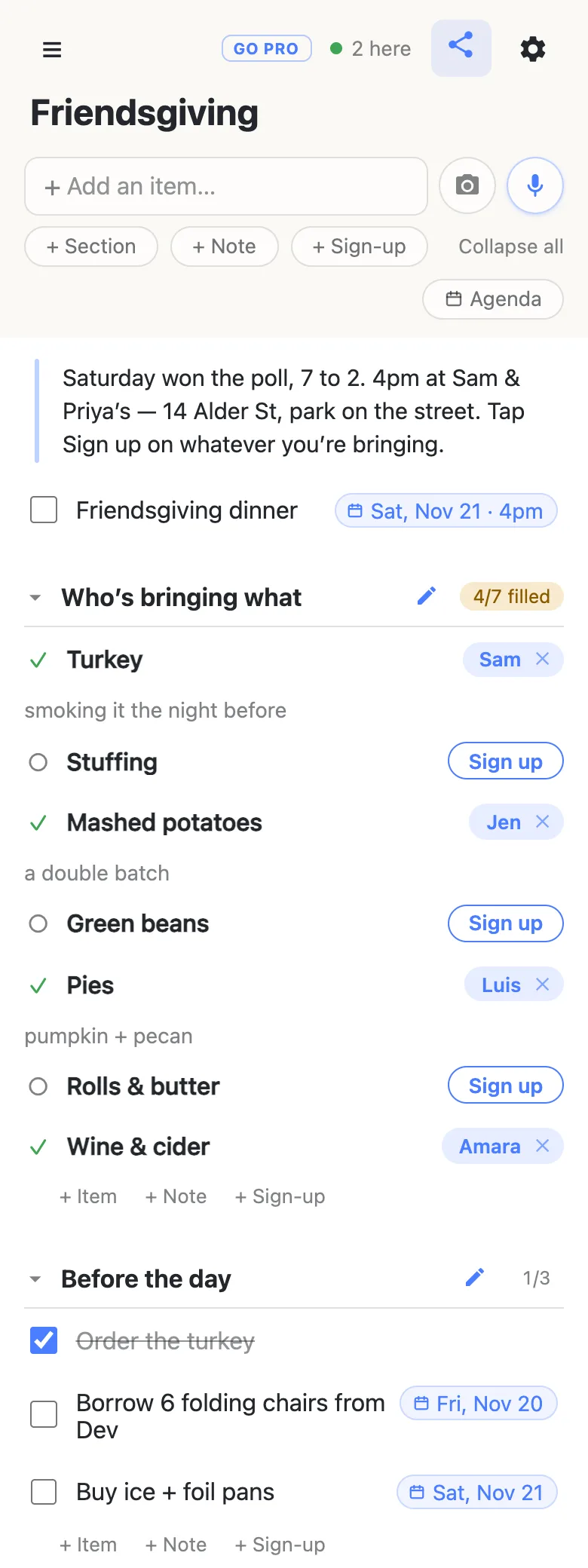 A phone showing a list titled “Friendsgiving” with a presence chip reading “2 here”. A note at the top reads “Saturday won the poll, 7 to 2. 4pm at Sam & Priya’s — 14 Alder St, park on the street. Tap Sign up on whatever you’re bringing.” Below it, a row “Friendsgiving dinner” carries a date chip reading “Sat, Nov 21 · 4pm”. A section headed “Who’s bringing what” shows a 4/7 filled counter: turkey claimed by Sam with the note “smoking it the night before”, stuffing open with a Sign up button, mashed potatoes by Jen noting “a double batch”, green beans open, pies by Luis noting “pumpkin + pecan”, rolls and butter open, and wine and cider by Amara. A second section, “Before the day”, reads 1/3: “Order the turkey” ticked and struck through, “Borrow 6 folding chairs from Dev” dated Fri, Nov 20, and “Buy ice + foil pans” dated Sat, Nov 21.