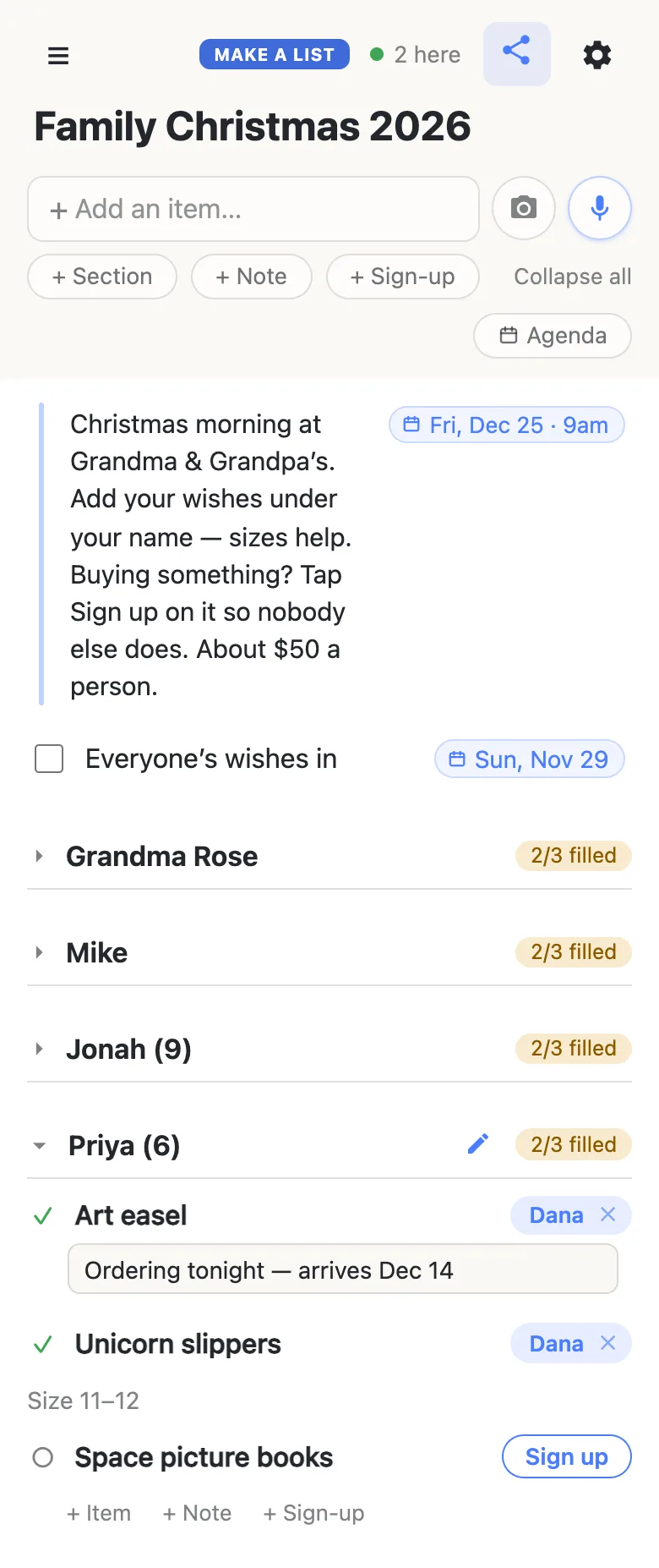 Aunt Dana’s phone showing the same Family Christmas 2026 list, with a green dot and “2 here” in the header. The note with its Fri, Dec 25 · 9am chip and the “Everyone’s wishes in” row dated Sun, Nov 29 sit at the top. Grandma Rose, Mike and Jonah (9) are folded shut, each reading 2/3 filled. Priya (6) is open and reads 2/3 filled: Dana has just signed up for the Art easel and is typing “Ordering tonight — arrives Dec 14” into the box beneath it; she also has the Unicorn slippers (“Size 11–12”), and Space picture books shows a Sign up button.
