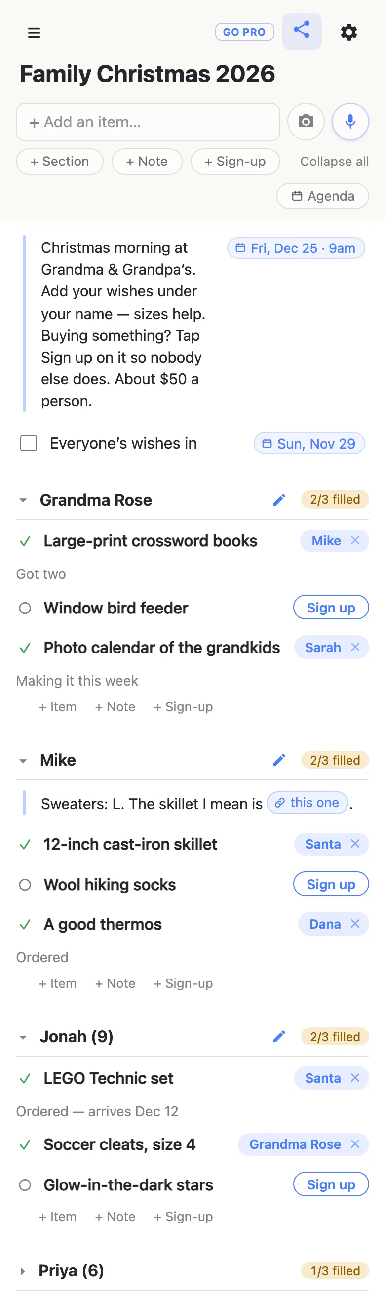 A phone showing a list titled “Family Christmas 2026”. A note at the top, with a date chip reading Fri, Dec 25 · 9am, says: Christmas morning at Grandma & Grandpa’s. Add your wishes under your name — sizes help. Buying something? Tap Sign up on it so nobody else does. About $50 a person. Below it, a checkbox row “Everyone’s wishes in” carries a chip reading Sun, Nov 29. The section Grandma Rose reads 2/3 filled: Mike has the Large-print crossword books (“Got two”), Sarah the Photo calendar of the grandkids (“Making it this week”), and Window bird feeder shows a Sign up button. Mike’s section, 2/3 filled, opens with a note — “Sweaters: L. The skillet I mean is” followed by a link chip labelled “this one” — then the 12-inch cast-iron skillet claimed by Santa, Wool hiking socks with a Sign up button, and A good thermos claimed by Dana (“Ordered”). Jonah (9), 2/3 filled: the LEGO Technic set claimed by Santa (“Ordered — arrives Dec 12”), Soccer cleats, size 4 claimed by Grandma Rose, and Glow-in-the-dark stars still open. Priya (6), 1/3 filled, is folded shut.