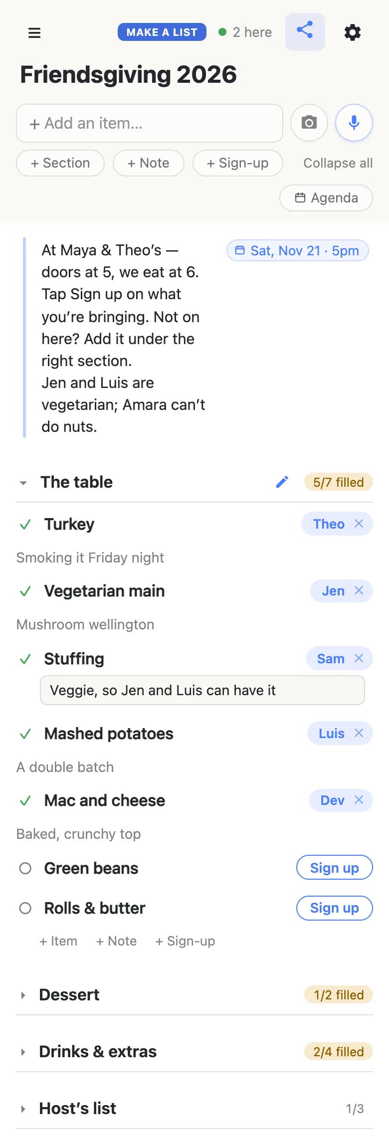 A friend’s phone showing the same Friendsgiving 2026 list, with “2 here” and a green dot in the header. The note and its Sat, Nov 21 · 5pm chip sit at the top. The table is open and now reads 5/7 filled: Sam has just signed up for the Stuffing and is typing “Veggie, so Jen and Luis can have it” into the note box beneath it; Theo, Jen, Luis and Dev still hold their dishes, and Green beans and Rolls & butter show Sign up buttons. Dessert (1/2 filled), Drinks & extras (2/4 filled) and Host’s list (1/3) are folded shut.